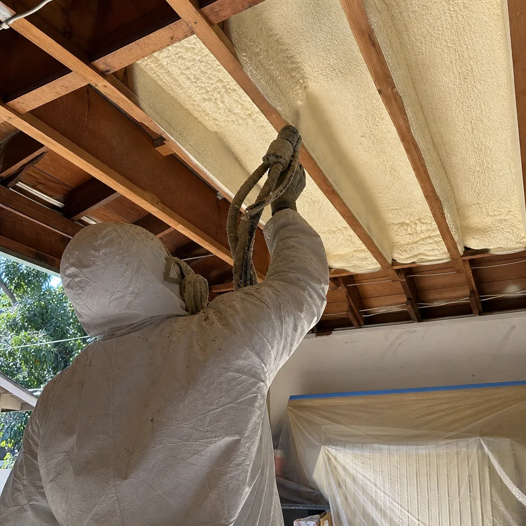 Contractor applying spray foam insulation to a wooden ceiling frame